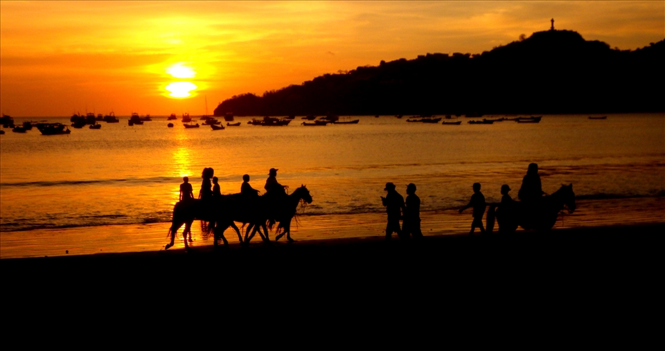 Horseback riders silhouetted against a golden beach sunset 