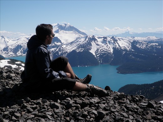 Hiker atop of The Black Tusk overlooking Garibaldi Lake on a clear day.