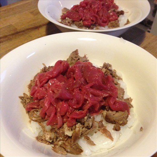 Raw beef and meat off the bone on top of noodles.