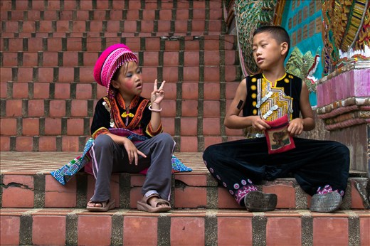 Chiang Rai, children with tradtional dress talk on the stairs of a temple