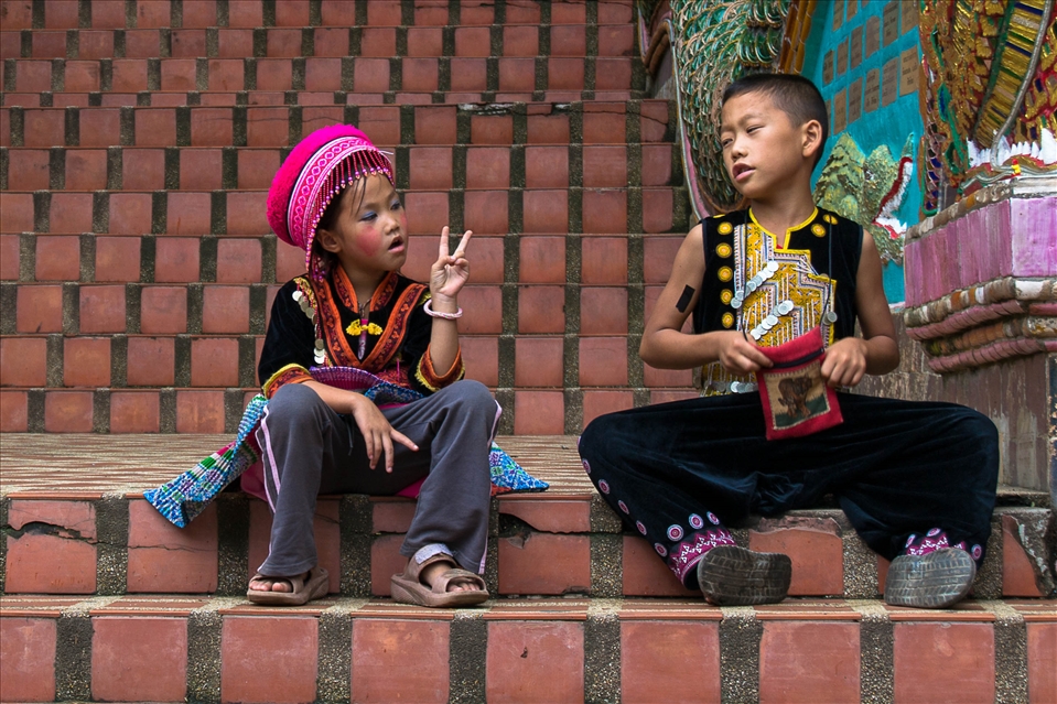Chiang Rai, children with tradtional dress talk on the stairs of a temple
