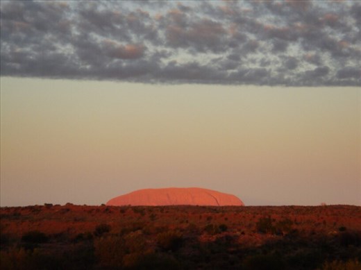 Uluru lights up at dawn while everything else remains shrouded in the dark