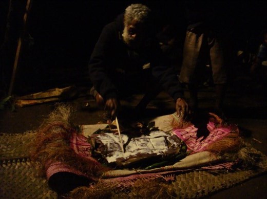 Head of the family cutting up taro laplap and chicken on kastom mats, hereby adopting me and Daniel, Lombaha, Ambae.