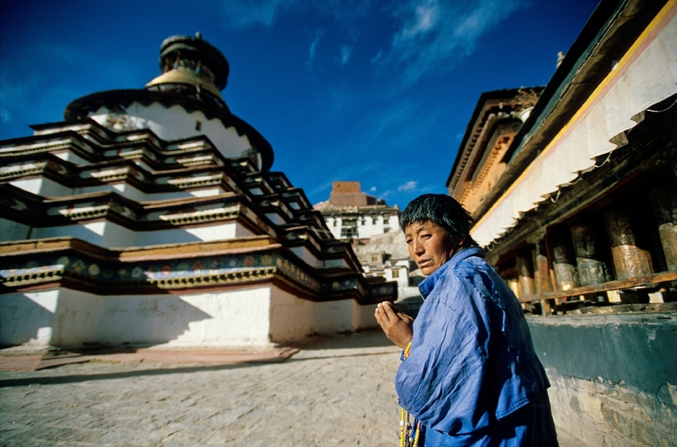 A female Tibetan pilgrim doing kora around the Gyantse Kumbum. The Kumbum or great gomang (many-doored) chorten at Gyantse is a three dimensional mandala, meant to portray the Buddhist cosmos. The Kumbum, like other mandalas, which are portrayed by a circle within a square, enables the devotee to take part in the Buddhist perception of the universe and can depict one's potential as they move through it. Mandalas are meant to aid an individual on the path to enlightenment.Gyantse, Tibet.