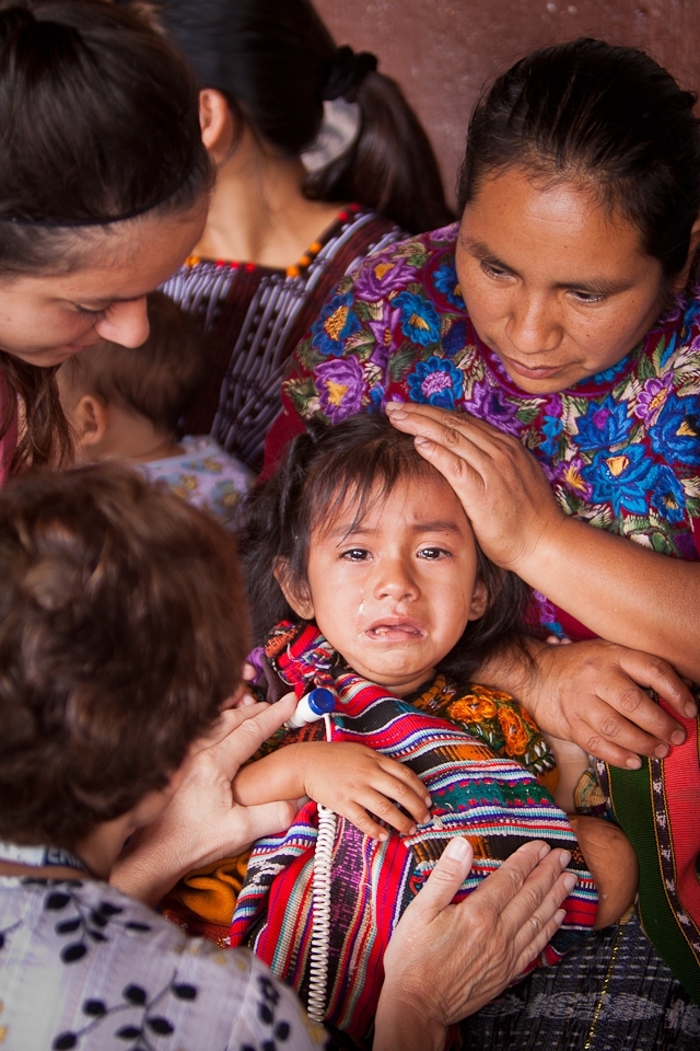 This young girl broke out crying while being treated for a sickness at the medical clinic. Two doctors and the girl's mother were quick to care for the ill child.
