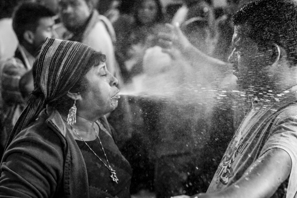 A shaman spits schnapps in the face of a man in a cleansing ritual that also includes being hit by seven different herbs and drinking a shot. Maximon has a weakness for alcohol and so the most common offering is a bottle of schnapps or beer, although money bills and fried chicken are popular alternative.