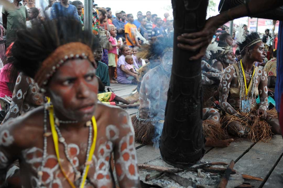 A man heats a drum among women in the Asmat Culture Festival. In their ritual beliefs, fire is something sacred. Their ritual activities always start by making a bonfire. Catholicism slowly replacing religious beliefs because it provides protection for the vulnerable acts of violence, especially for women and children. Asmat women are easier to believe in the Catholic teachings than their men.