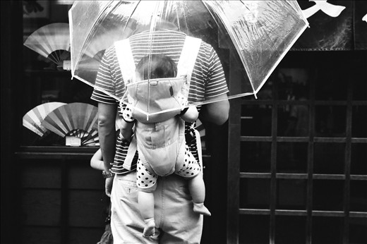 A little child, though young, already mimics his father’s stance as he peers out from underneath the shelter of the umbrella. 

