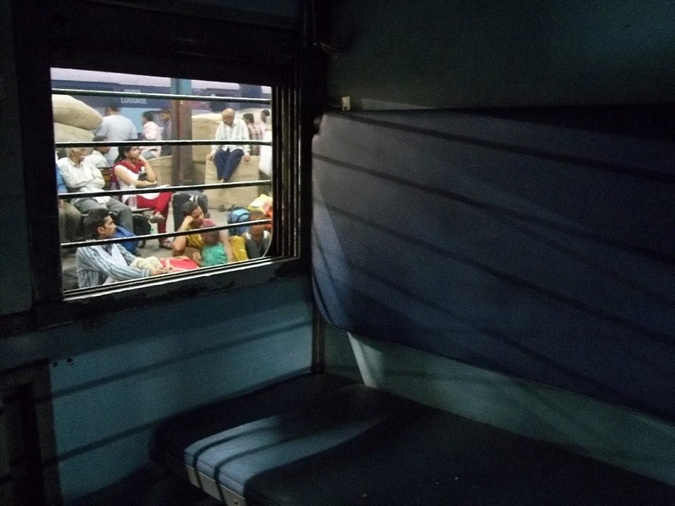 In the scene above we can see people are waiting for their respective journey to start. All are waiting either on the ground(family of husband and wife and their two kids), on benches(lady and an old man), and on the  luggage(which is to be loaded by coolies in the luggage compartment of the train on the next platform). Its a typical scene of an Indian Railways platform.
