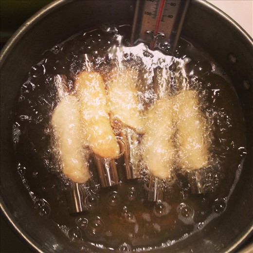 Cannolis frying to a crispy golden brown.