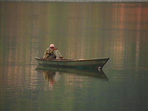 .- A man is fishing with a net on a boat in Pokhara, Nepal.
