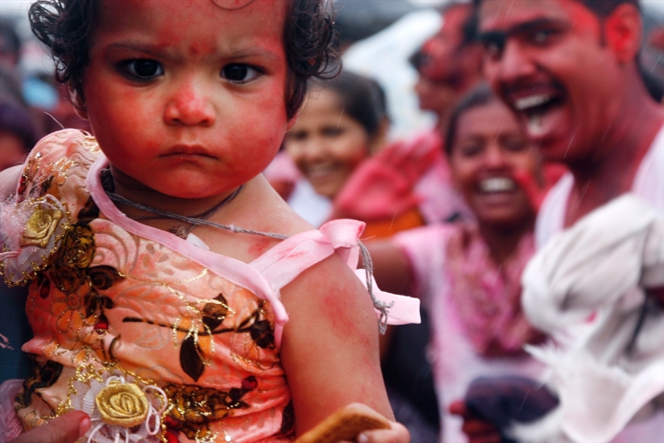 A family celebrates Ganesh Chaturthi Festival at Chowpatty Beach, Mumbai. During this celebration, many religous rituals are performed.  This includes offerings of food, flowers and coconuts to the statues of Lord Ganesh.  The most colorful offering is that of red powder.  While people offer the red powder to the Ganesh statues, they also throw it on people as well.