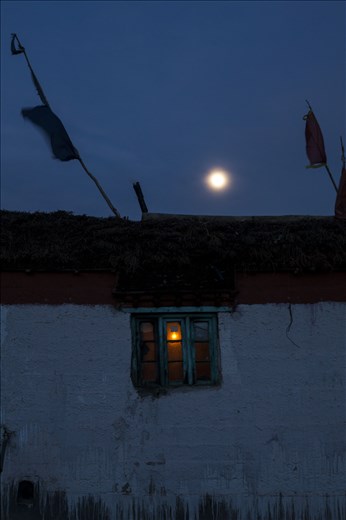 A traditional mud brick house, painted with a lime wash, prayer flags on roof
