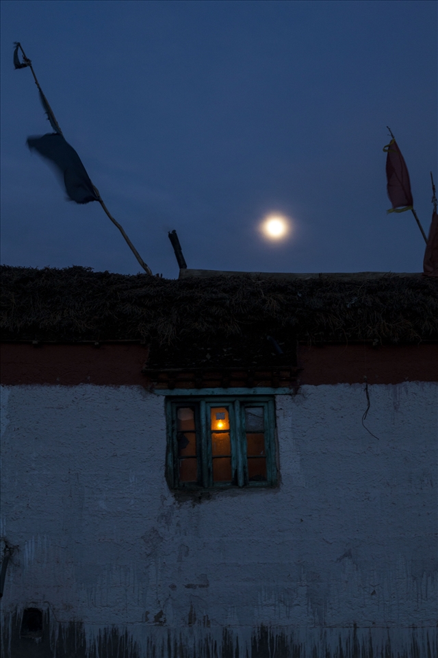 A traditional mud brick house, painted with a lime wash, prayer flags on roof