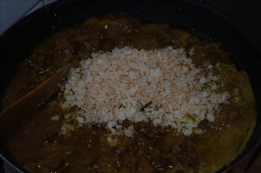 Adding coconut flakes to rendang