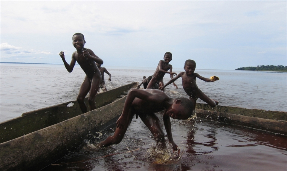 Boys playing on the shores of lake Mai Ndombe whilst their mothers and sisters do the laundry nearby.