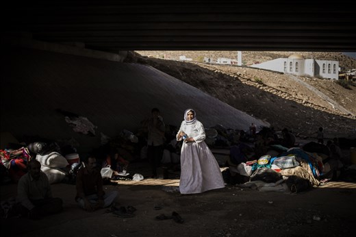 An elderly Yazidi woman walks among a makeshift camp under a motorway bridge.