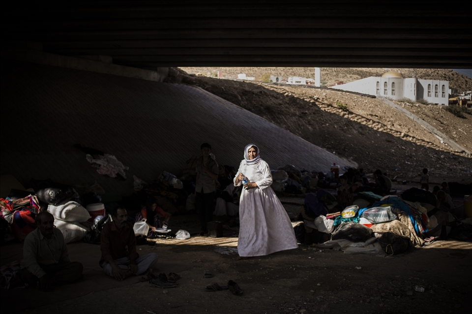 An elderly Yazidi woman walks among a makeshift camp under a motorway bridge.
