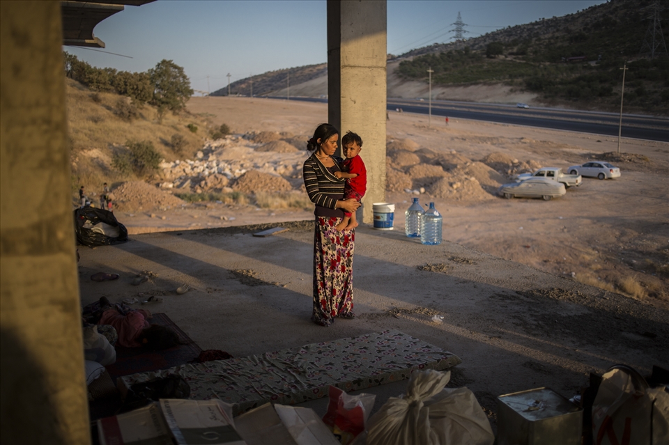 A young Yazidi mother carries her child in her arms inside an unfinished buildi