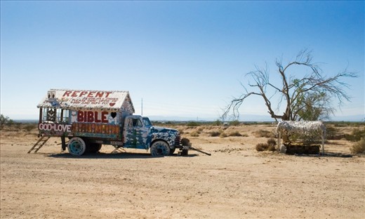 An old truck and shade structure with a bed, both used as areas of refuge from the hot desert sun for by Leonard when needing a break during his building.