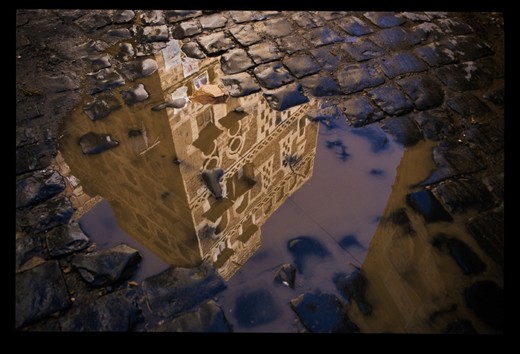 A momentary reflection of a traditional Yemeni towerhouse and it's political posters in a puddle  over the cobblestones. Political posters of President Saleh can be seen, a man whose own world would be turned upside down during the Arab Spring.