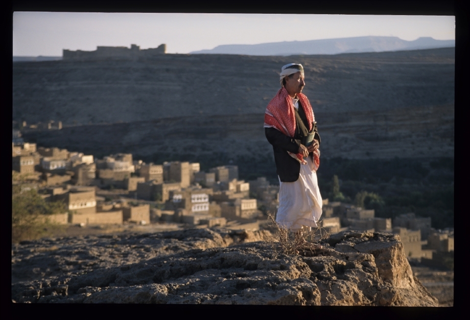 A Yemeni villager surveys his homeland, the ancient fortress above that once protected the valley and his village below, glowing in the last beams of the sun to penetrate the narrow gorge.Within a few years his long-time president will be ousted and US drone strikes will threaten this tranquil landscape.