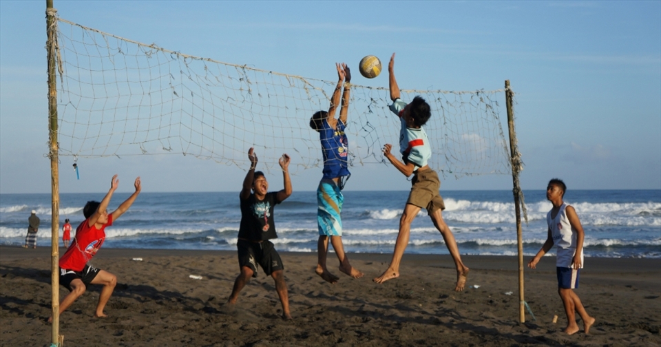 Several youth were playing beach volleyball. they were a fisherman and they are playing volleyball for waiting off to the sea.