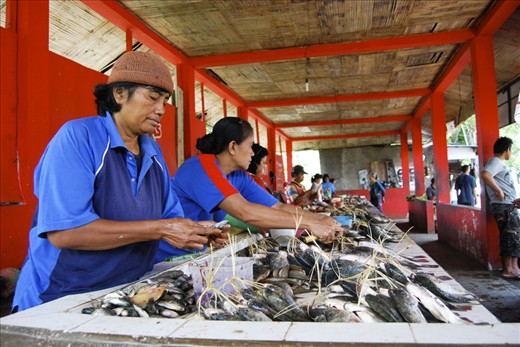 Fishmongers lined up at a long table, preparing the fishes for potential buyers. Side by side, they cut and clean fishes using a pair of skilled hands.