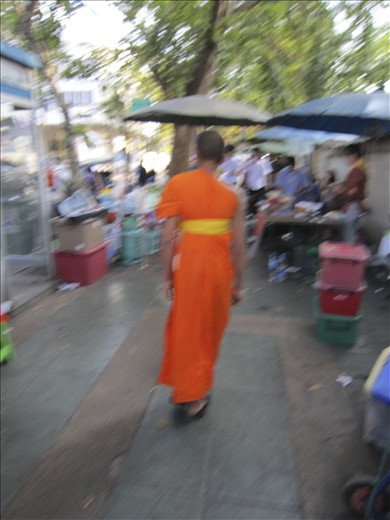 Contemplation amid the rush; young Thai monk walks among street vendors.