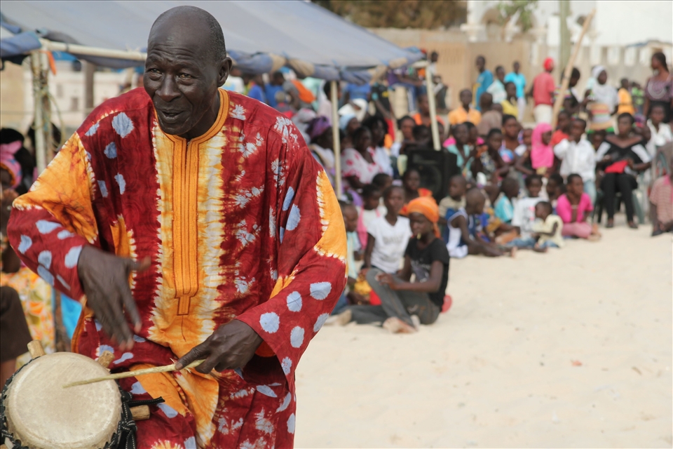 The griot is teaching the youth about the tradition of the Sabar drum.