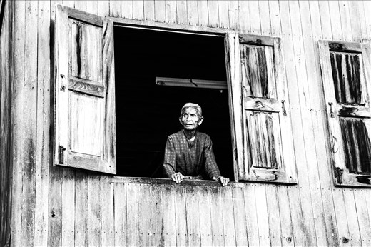 An elderly woman stands in her window to the world. (Myanmar)