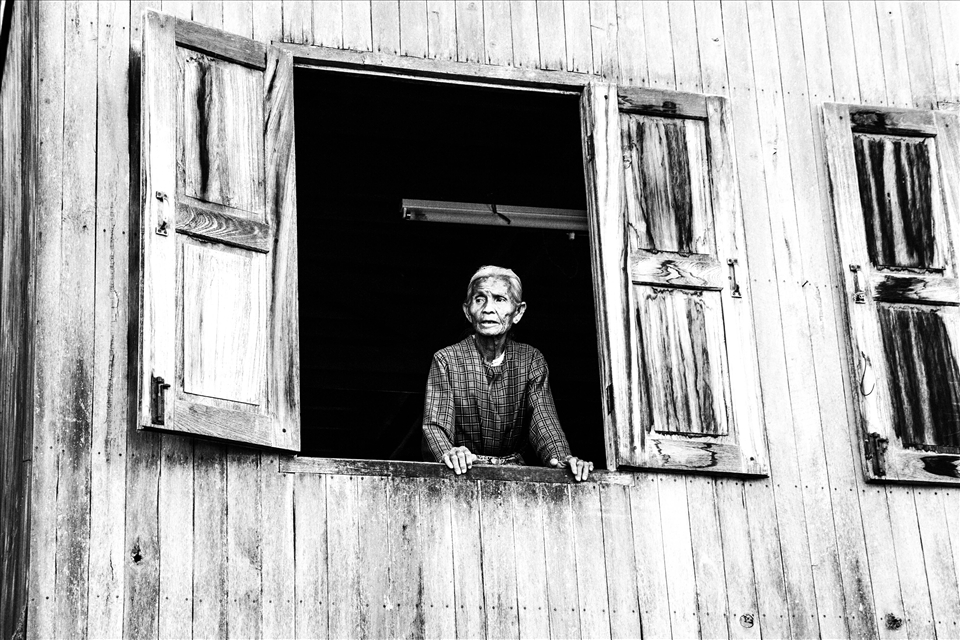 An elderly woman stands in her window to the world. (Myanmar)