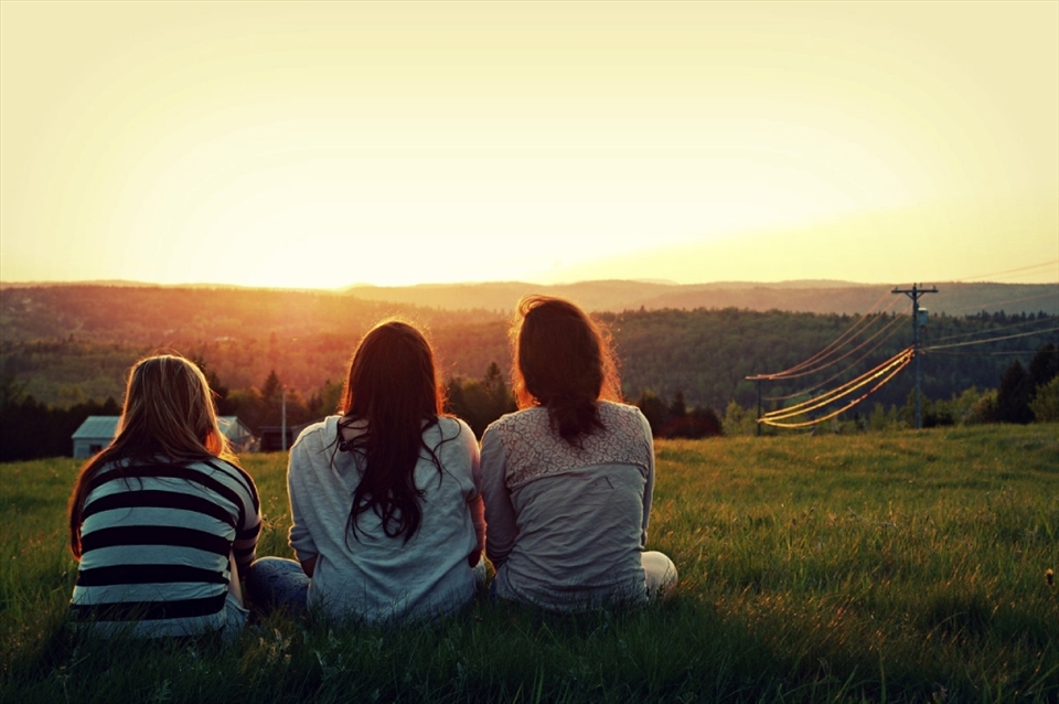Three friends run up a massive elevated field of grass behind their farm to catch the sunset as the sun falls behind the mountains to finalize a beautiful day. 