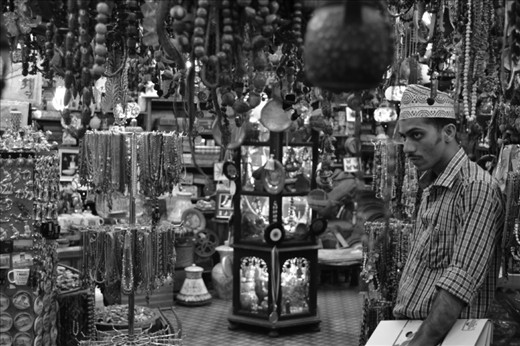 This salesman closely watches the tourists to avoid any theft of the innumerable pieces of traditional Omani ornaments and souvenirs.
