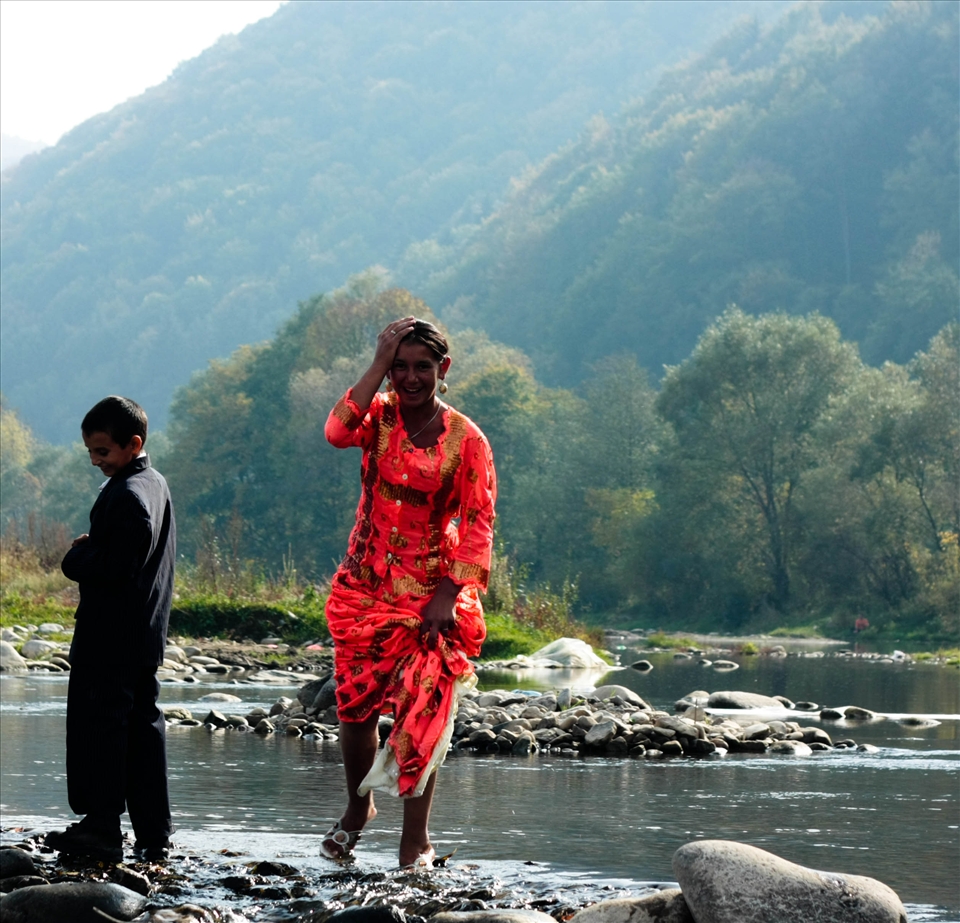 Gypsy girl crossing the creek in Negreni at the annual flea-market in October. Many gypsy families come to the market from afar, some of them still come by horses and carts. They sleep in tents in the nearby forests and wash in the creek by Negreni. This young girl looked like a wonder, so beautiful so I couldn't keep my eyes off her and when she crossed the creek, and most likely the cold water tickled her feet, I managed to captured her smile, which was shy and playful in the same time.