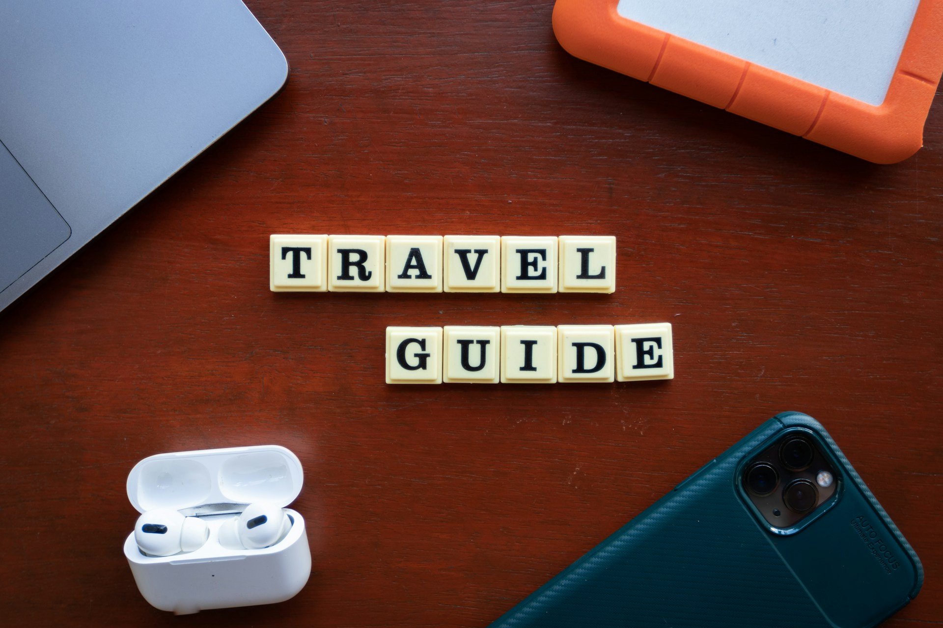 A wooden table with airpods, and block letters spelling 'Travel Guide'