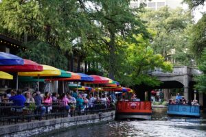 A group of people sitting at tables with umbrellas on the side of a river