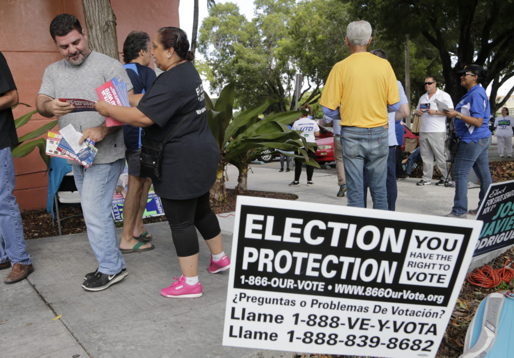 Ingrid Vaca of Virginia, a volunteer with Election Protection, hands a voter a leaflet informing him about voter's rights outside of a polling station at the Miami-Dade County Auditorium on Tuesday. (Lynne Sladky/AP)
