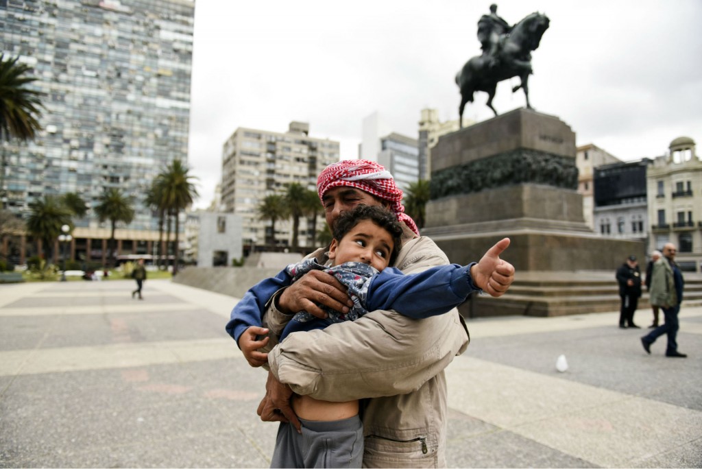 Un refugiado sostiene a su hijo en la Plaza Independencia, en Montevideo (AP)