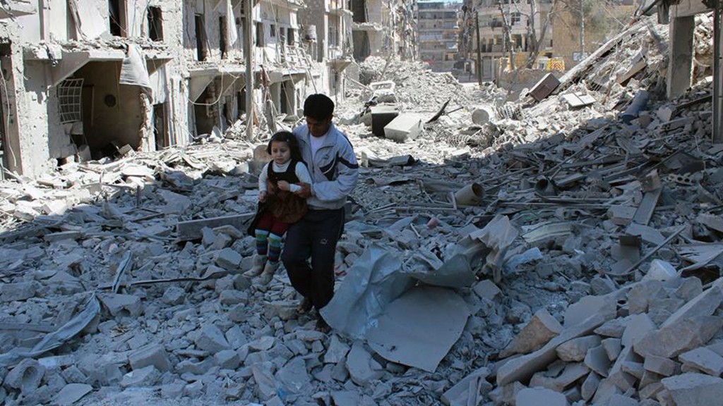 Un hombre sostiene a una niña en los escombros causados por los bombardeos del régimen de Bashar al Assad (AP)