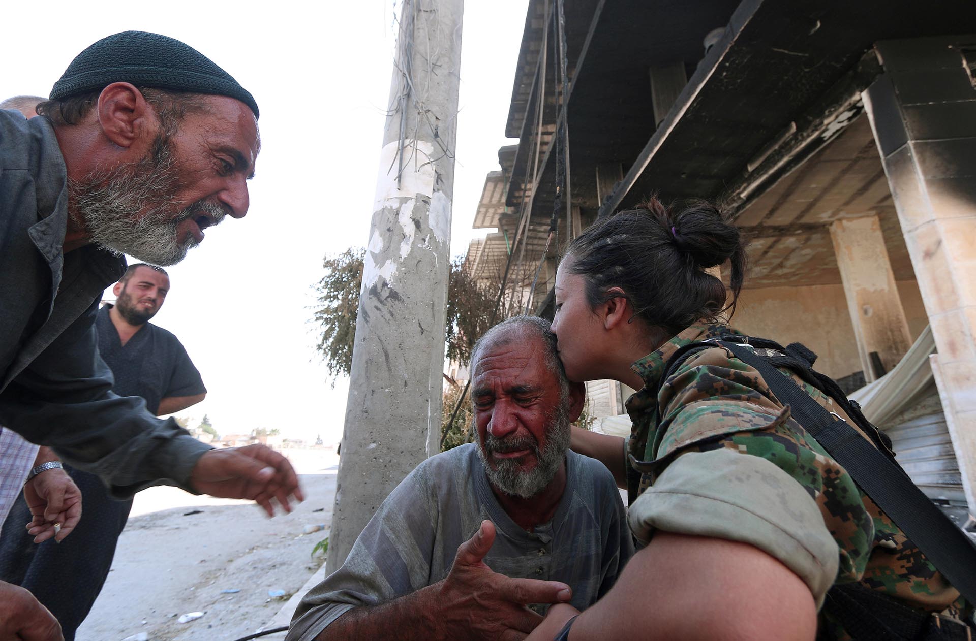 Una combatiente del SDF consuela a un hombre que comprueba que ISIS no está más en en hogar (Reuters)