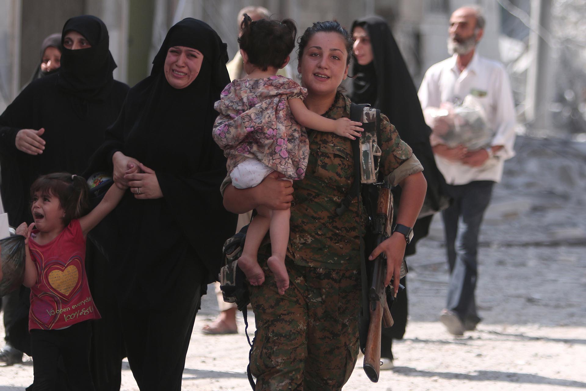 Una combatiente del SDF lleva a una niña, mientras la emoción de las mujeres es evidente al conocer que el Estado Islámico había sido expulsado de Manbij, en Alepo (Reuters)