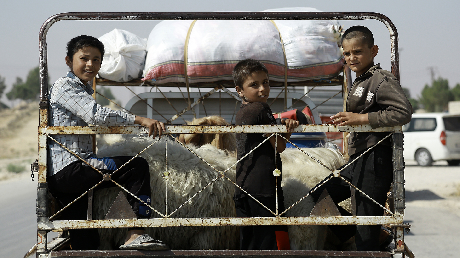 Niños sirios sentados detrás de una camioneta, en la ciudad siria de Manbij, donde los civiles regresan a sus casas después de que fuerzas árabes y kurdas expulsaran a ISIS/ (AFP)