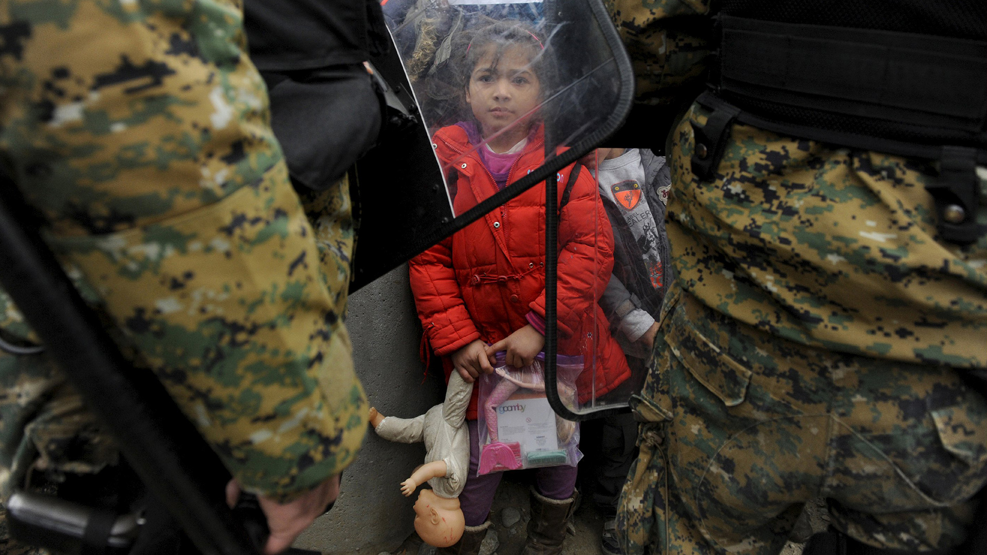 Una niña migrante sostiene sus juguetes mientras la policía Macedonia bloquea el paso en el límite con Grecia. REUTERS/Alexandros Avramidis