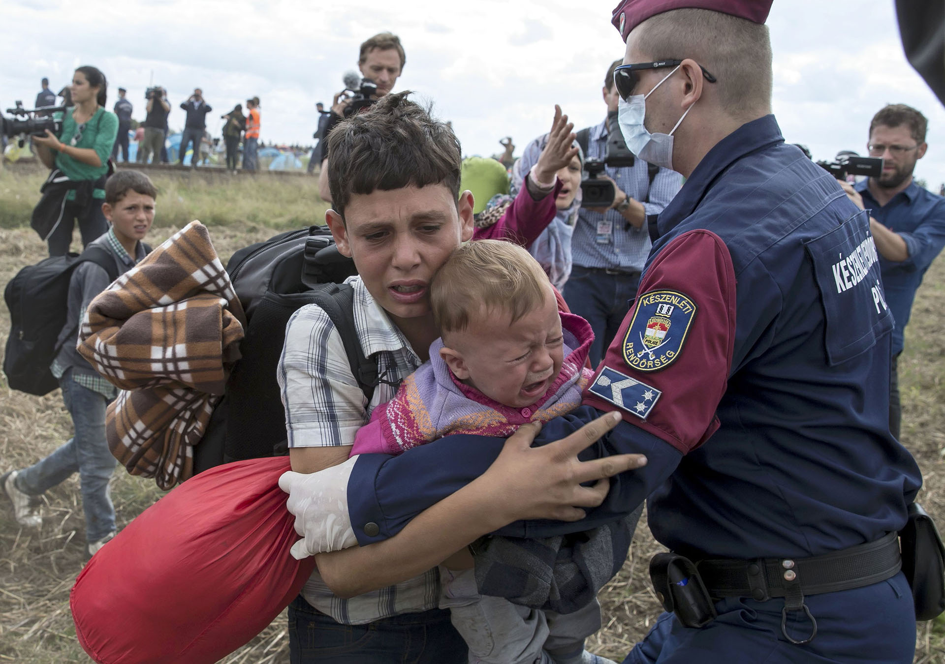 Un policía húngaro trata de detener a un niño migrante que corre cargando un bebé camino a un punto de encuentro. REUTERS/Marko Djurica TPX IMAGES OF THE DAY
