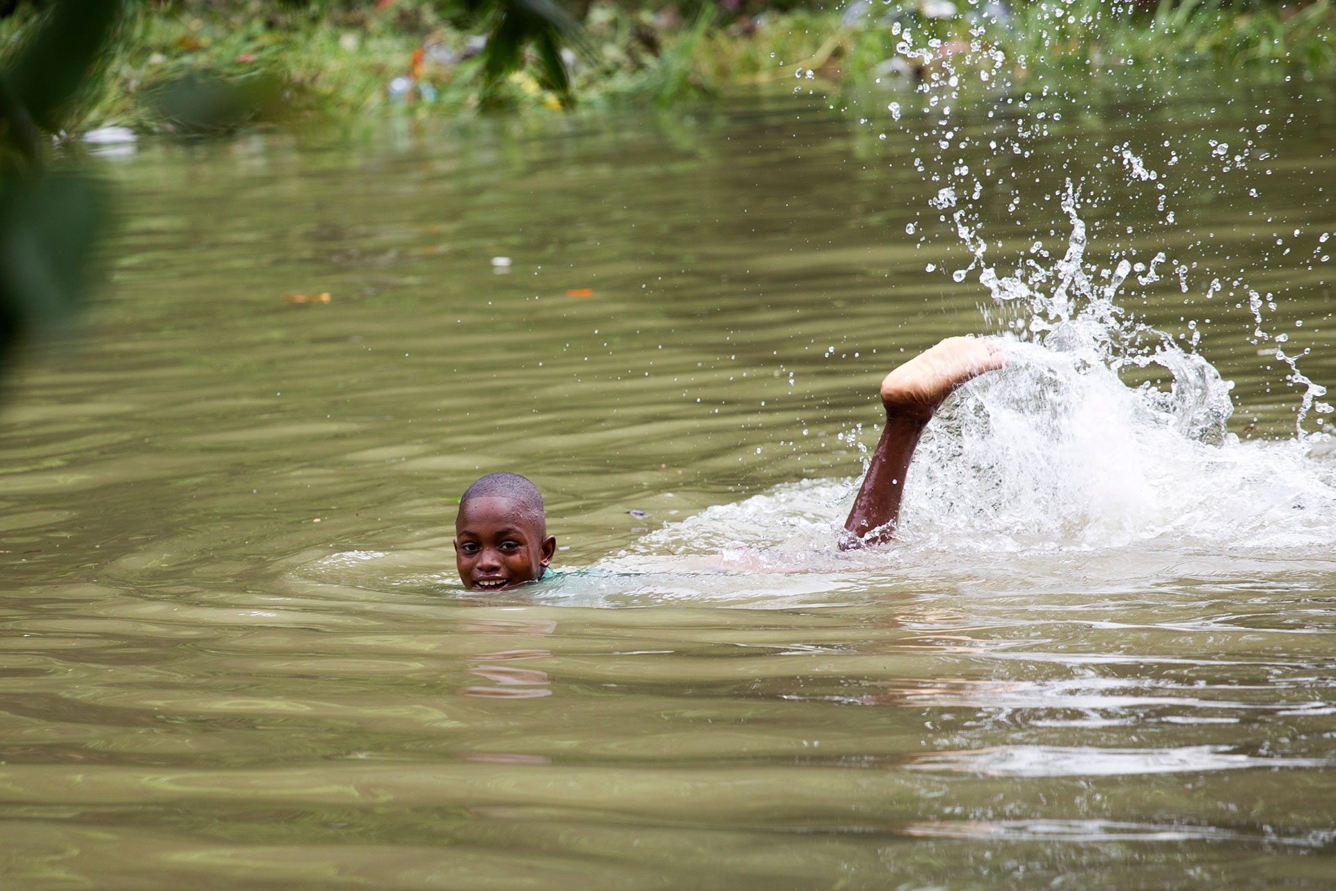 Un nió en Haití sonríe mientras nada en plena inundación (AFP)