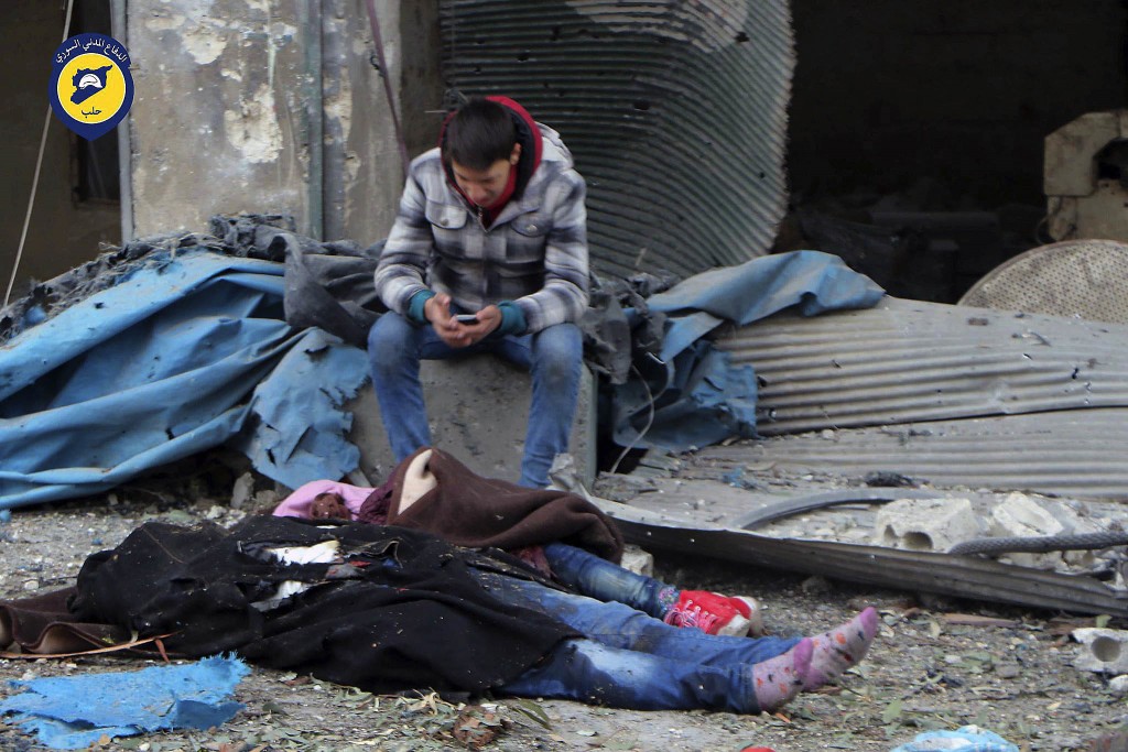 Un chico sentado cerca de cuerpos sin vida tras un ataque de la artillería en el distrito de Jub al-Quba en Alepo, este miércoles (Syrian Civil Defense White Helmets via AP)