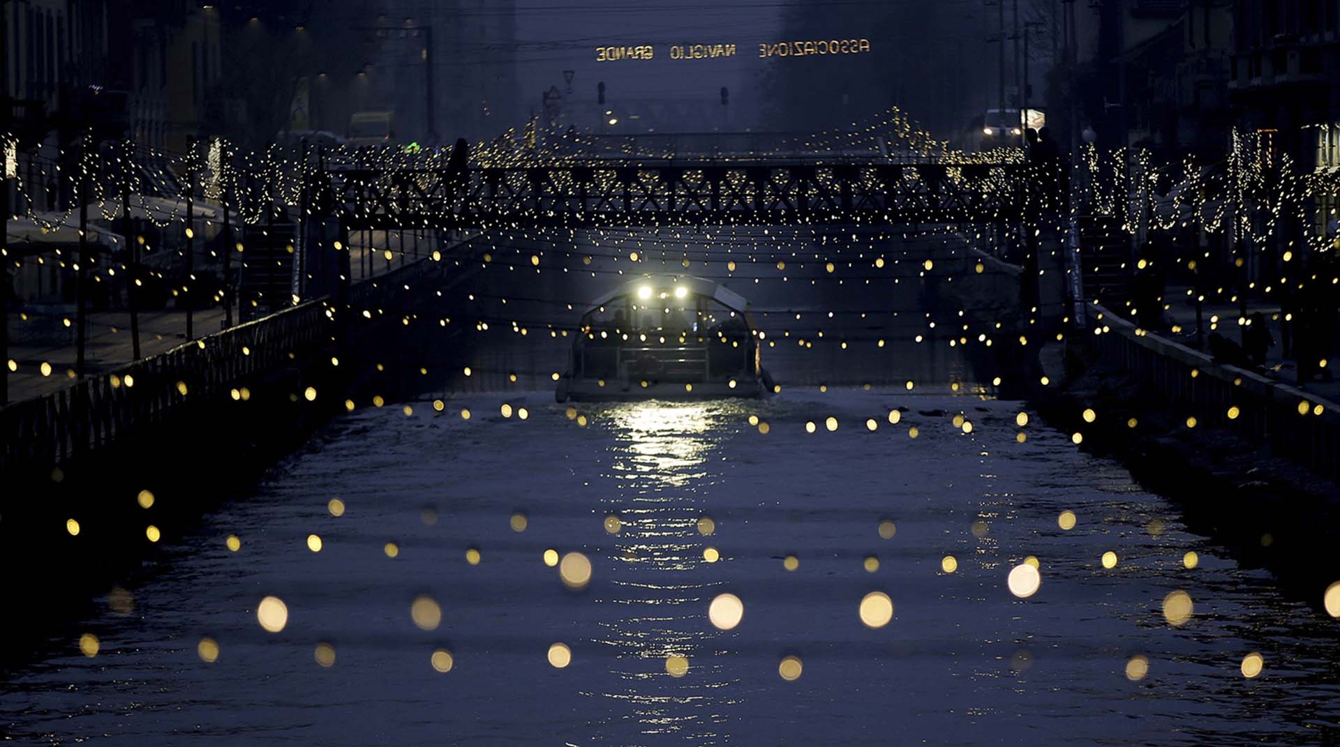 La Darsena dei Navigli iluminada ante el paso de un bote turístico, en Milán, Italia