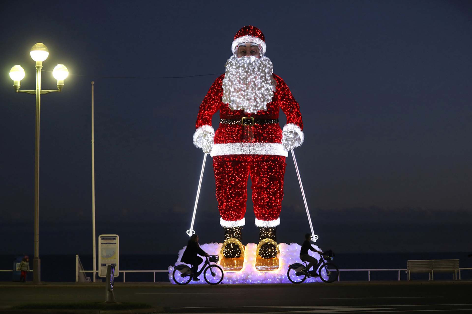Los ciclistas pasan por delante de un gigante modelo de Santa Claus iluminado a lo largo de la “Promenade des Anglais” en la ciudad de la Riviera francesa de Niza, Francia