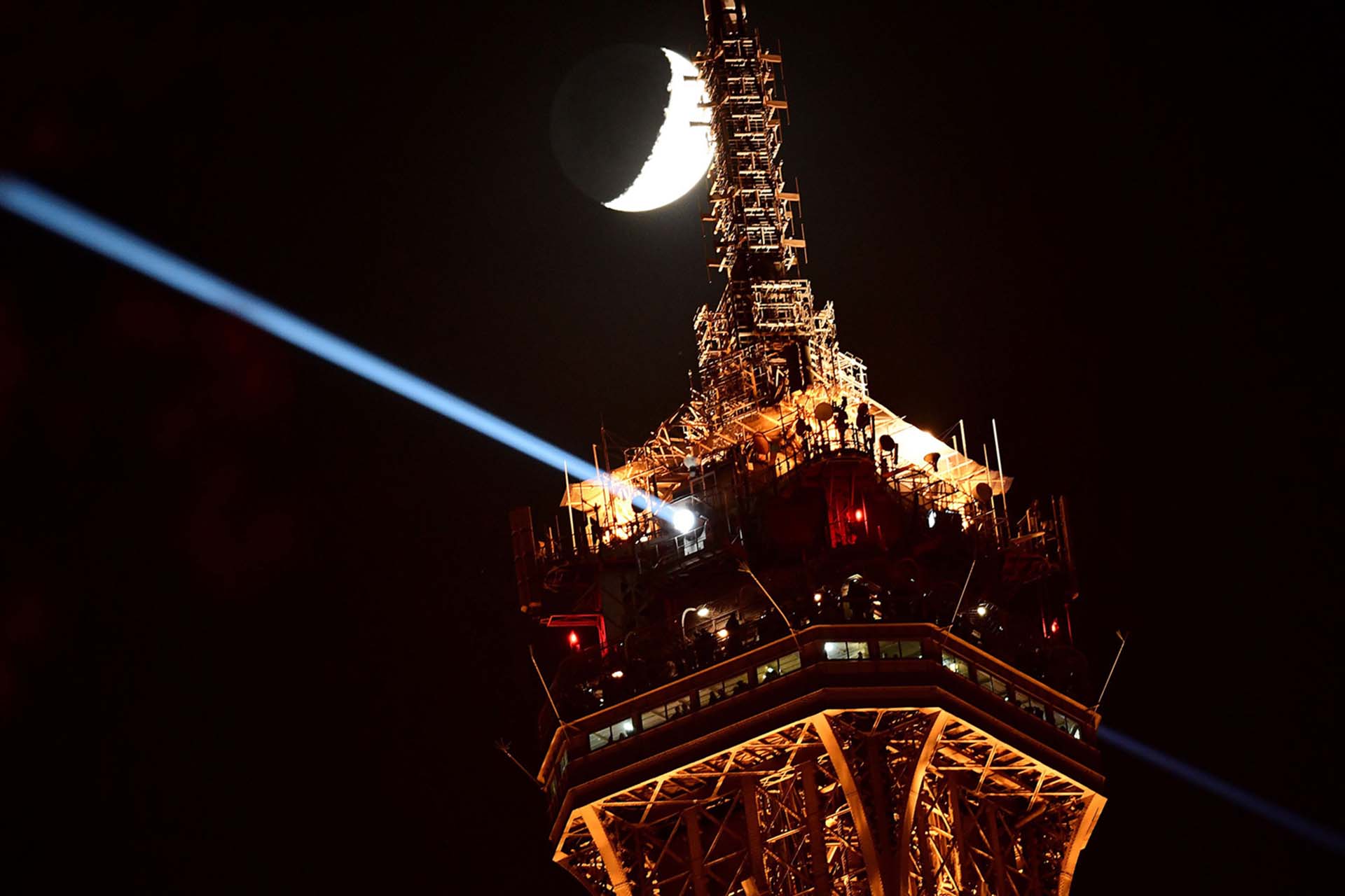 La luna creciente se ve al lado de la tapa de la torre Eiffel iluminada el 5 de diciembre de 2016 en París, Francia